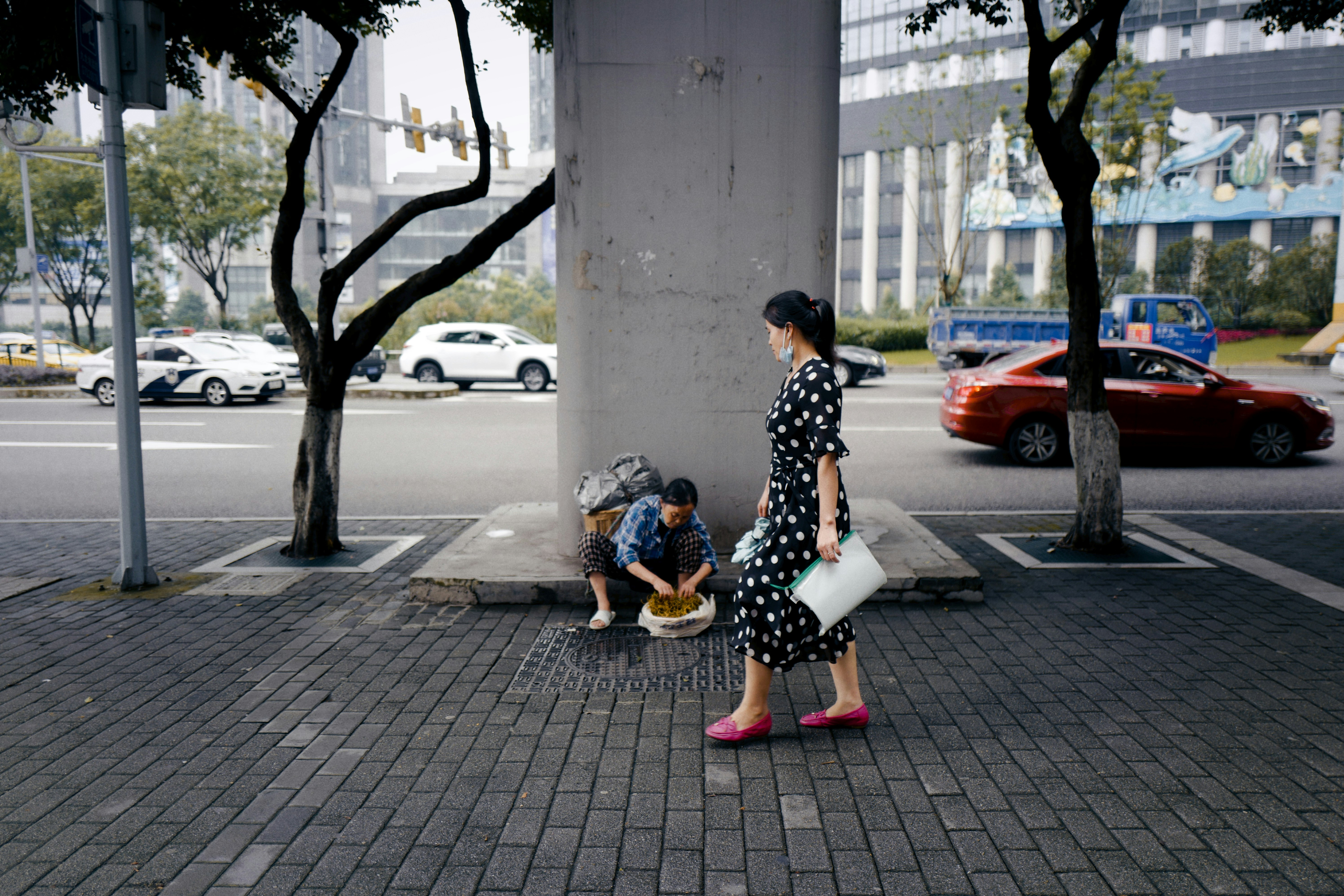 woman in black and white floral dress sitting on gray concrete pavement